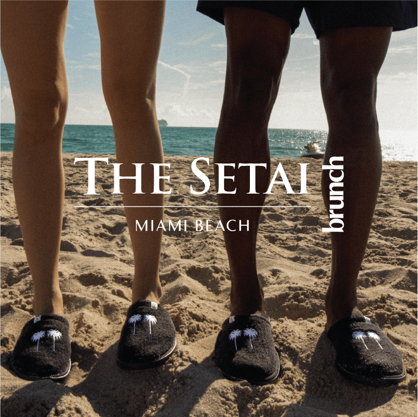 Front view of black Brunch slippers with white palm-tree embroidery on a sandy beach; overlaid text 'The Setai Miami Beach'