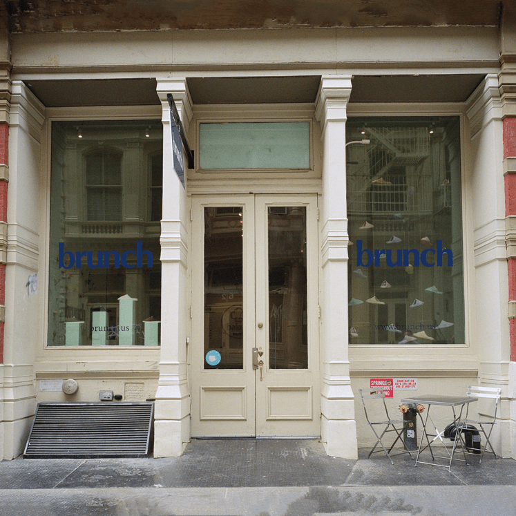 Brunch Soho storefront with beige double doors, blue 'brunch' window logos, shoe displays and a sidewalk table and chairs