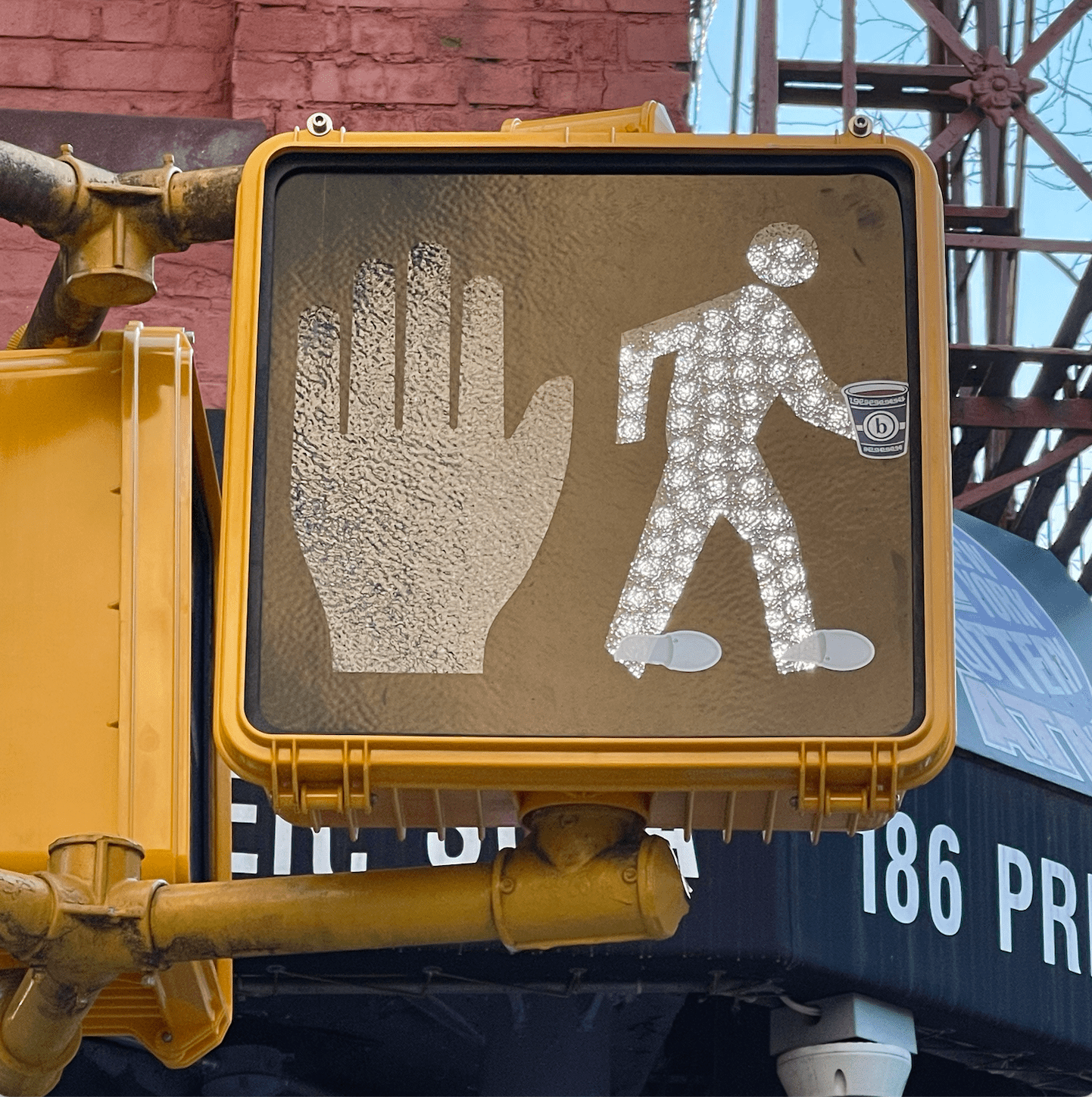Pedestrian signal showing stop hand and walking figure with a small Brunch cup sticker on a yellow signal box