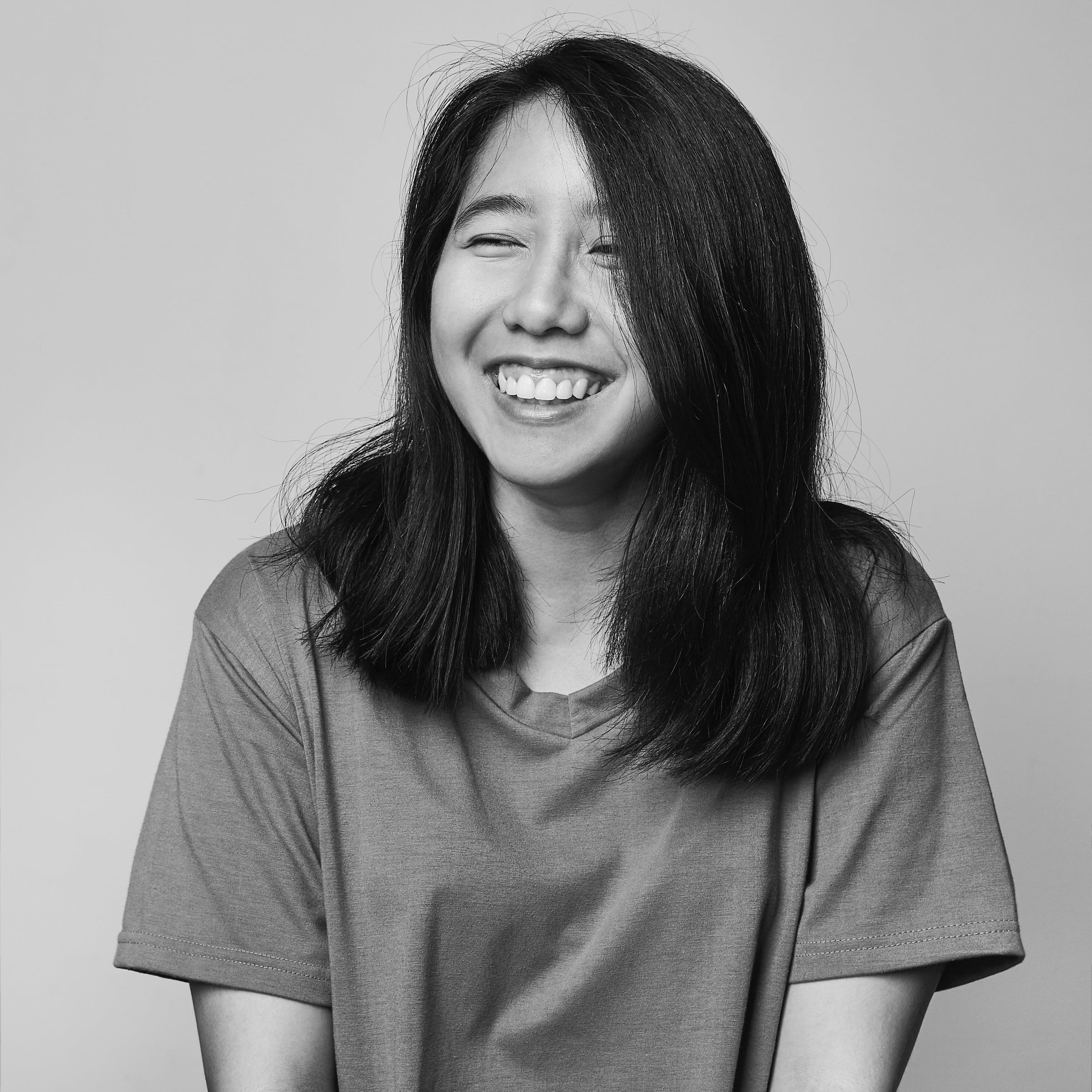 Smiling young woman laughing in a black-and-white studio portrait with a plain light background