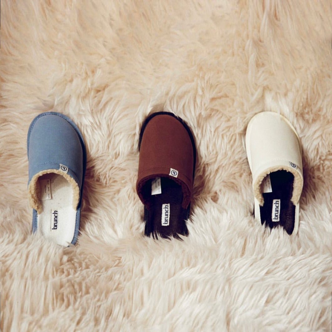 Top view of l'Essentiel slippers showing suede uppers and shearling lining in blue, brown and marshmallow on a rug