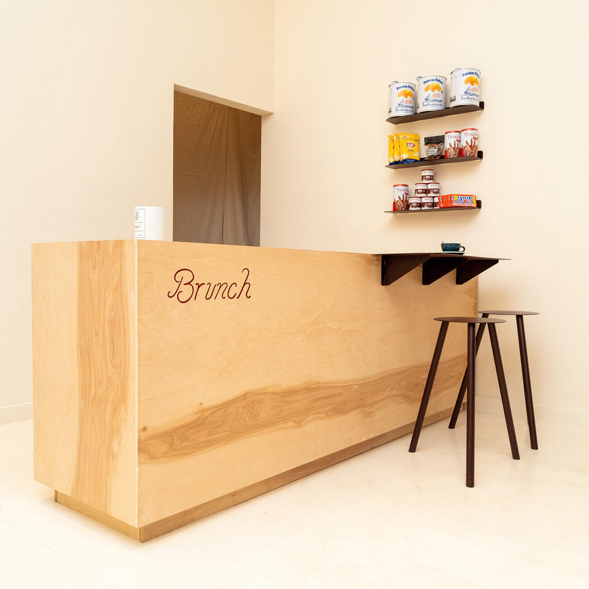 Minimal wooden café counter with 'Brunch' script, two tall stools and small snack shelves