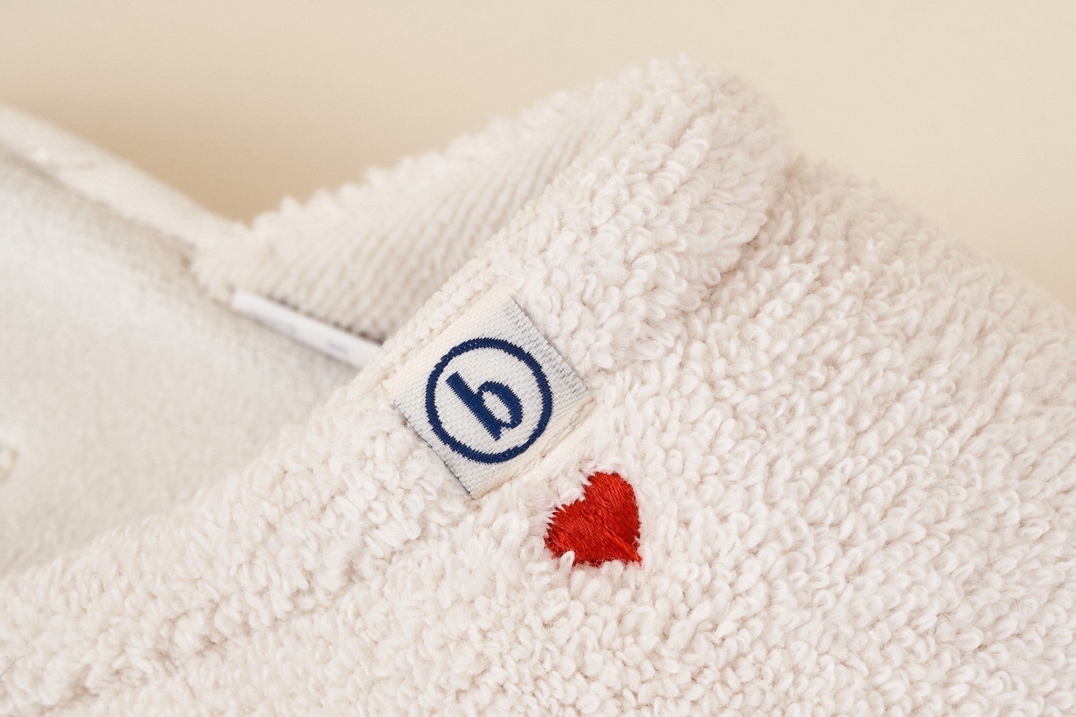 Close-up of cream Brunch slipper showcasing a red embroidered heart and brand logo tag on textured terry fabric