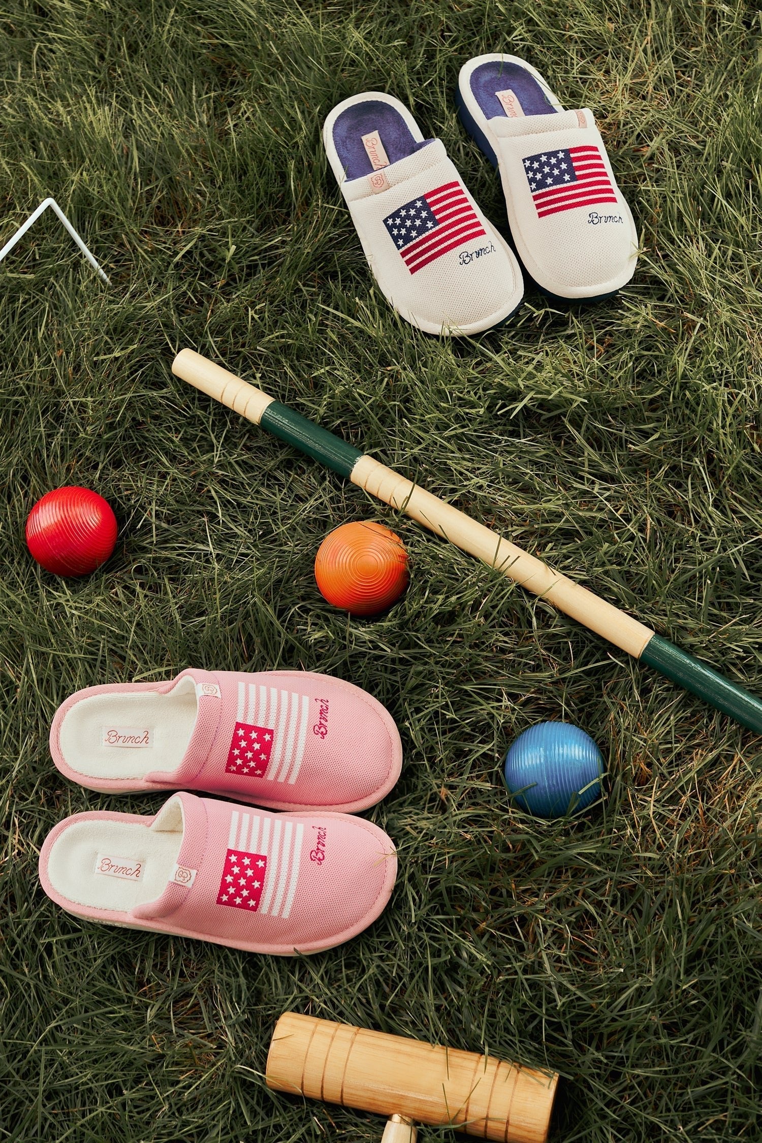 Top-down view of Essential knit slippers (beige and pink) showcasing embroidered American flag and Brunch script on grass