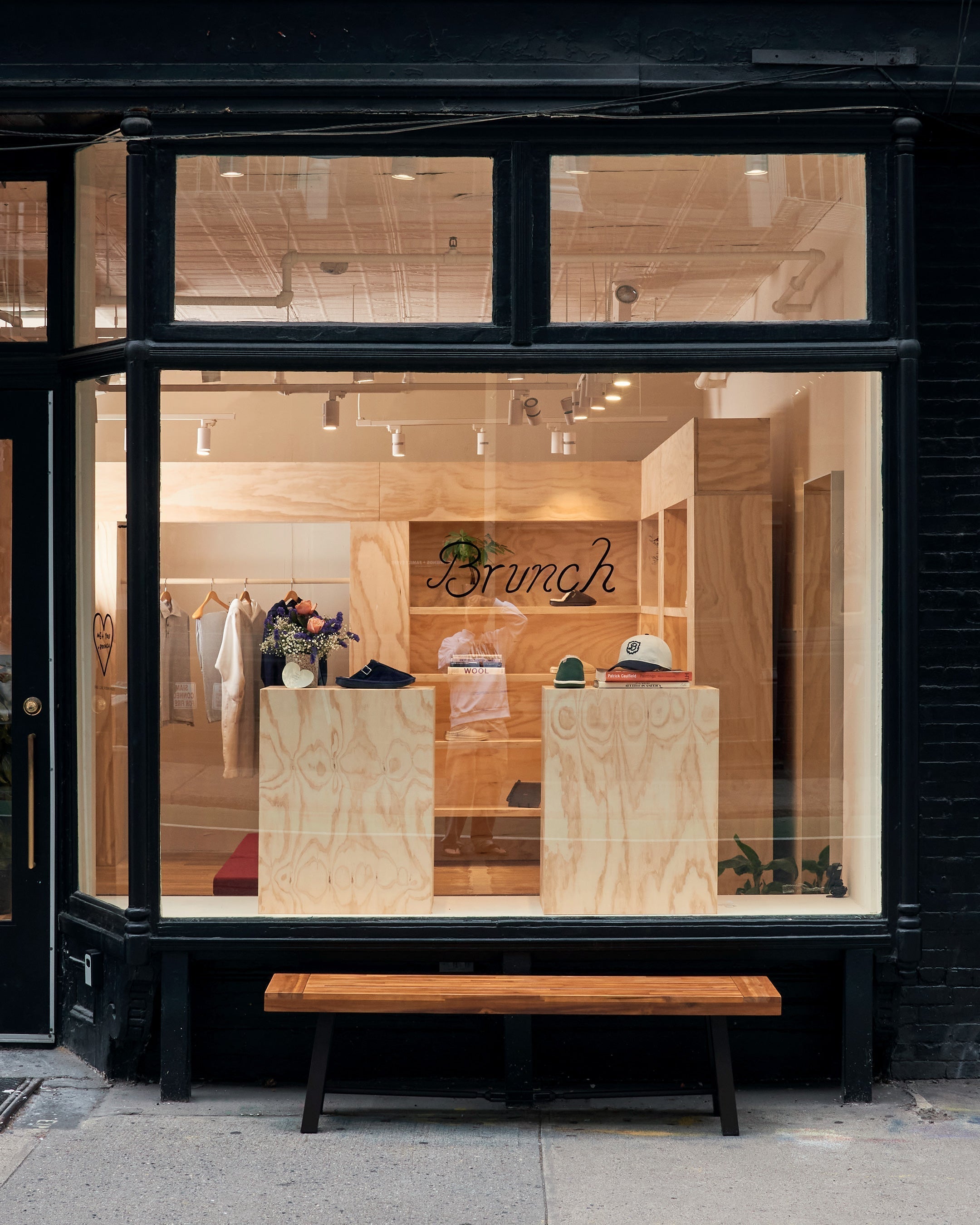 Shopfront window showing wooden displays with clothes, flowers and a handwritten 'Brunch' sign; folded shirt labeled WOOL