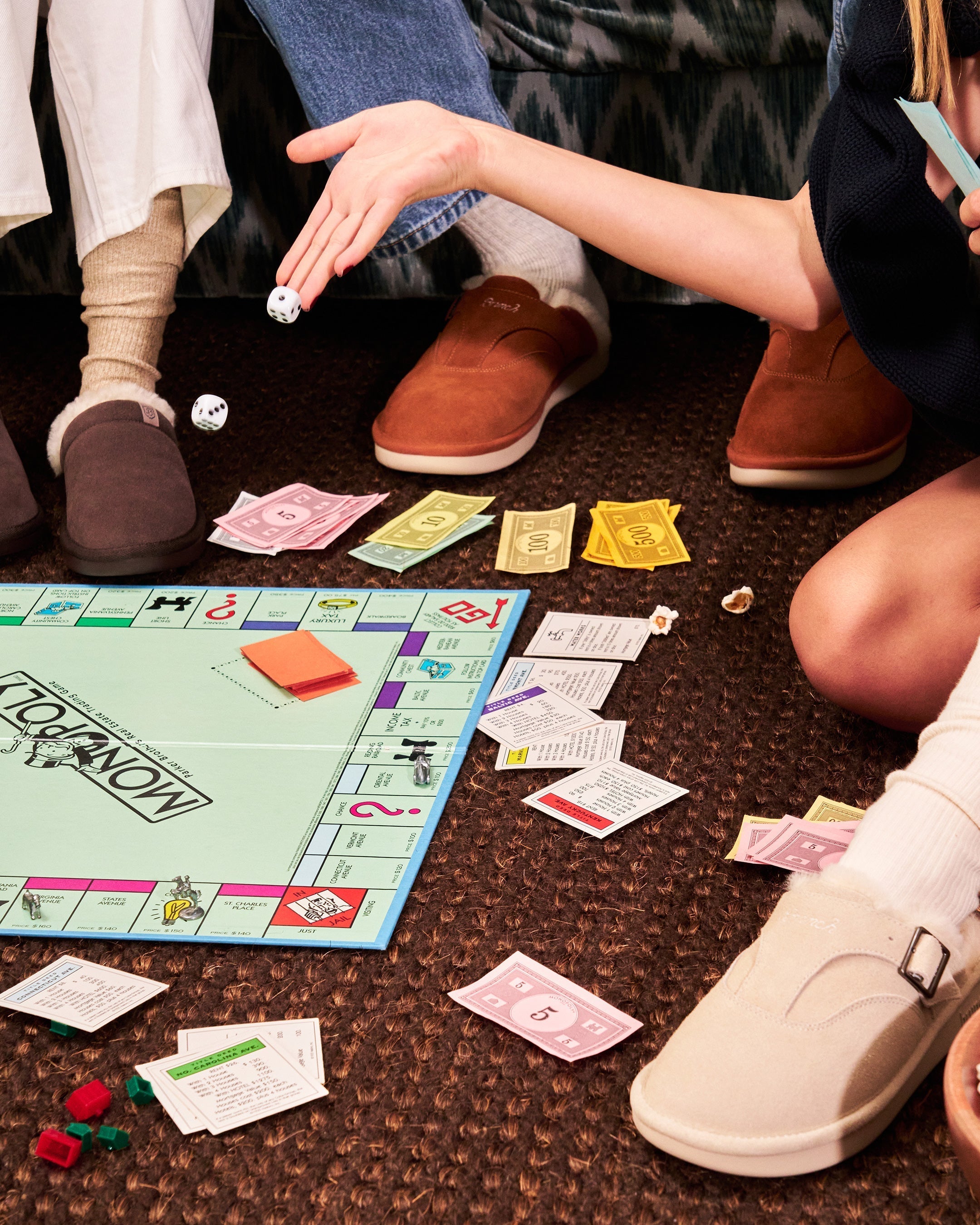 Two people playing Monopoly on a carpet while wearing tan and brown shearling-lined suede slip-on shoes