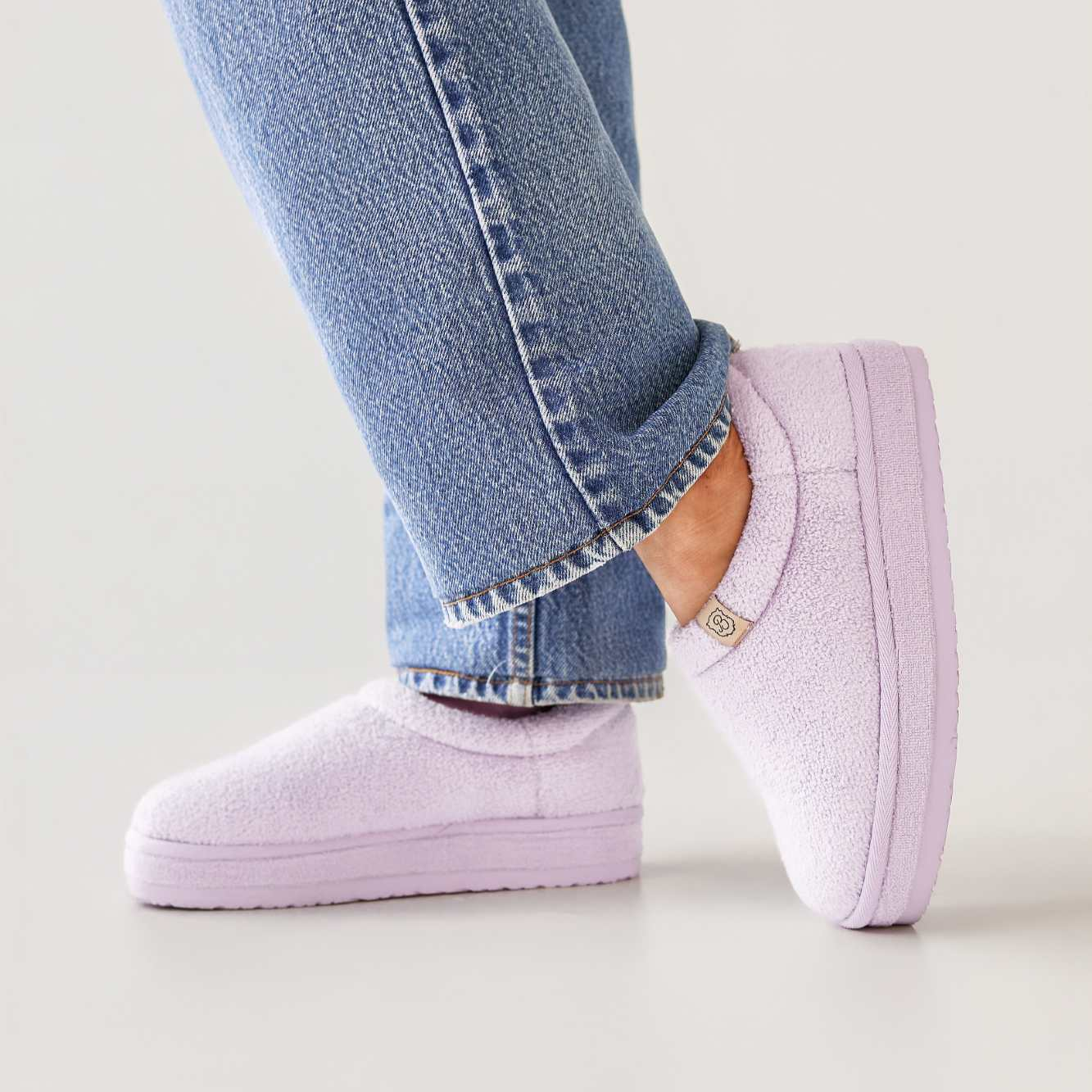 Person wearing light purple slip-on shoes with rolled-up blue jeans on a neutral background