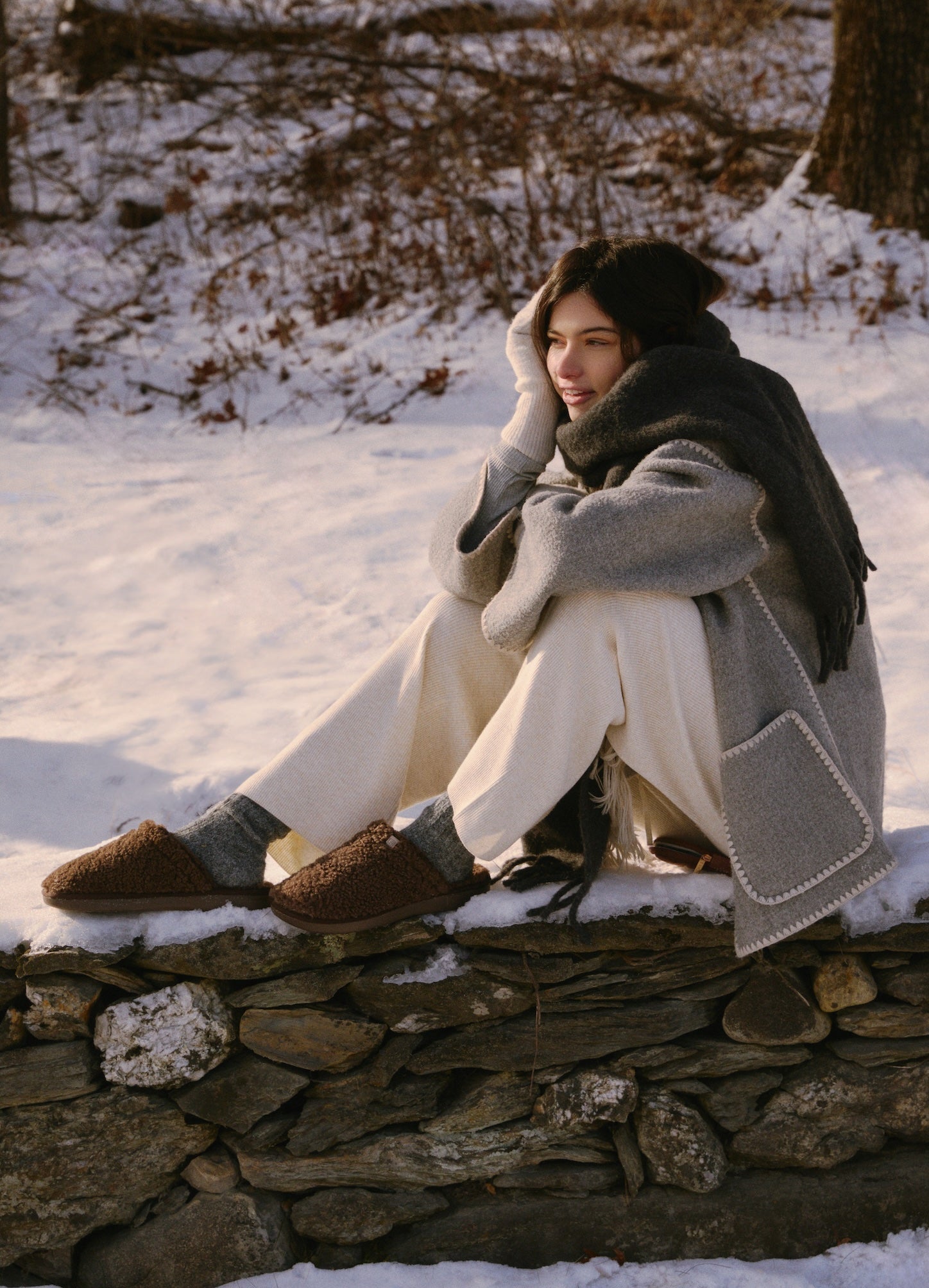 Person sitting on a stone wall in a snowy landscape