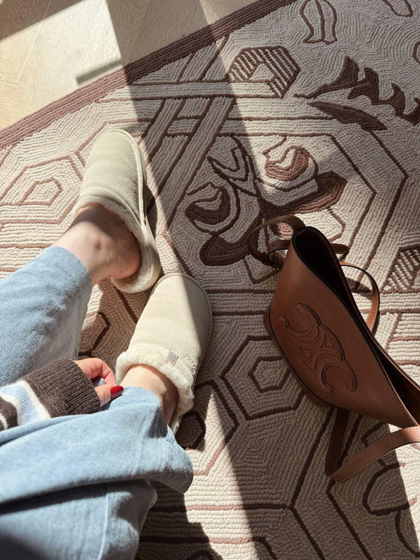 Top down view of Essential Shearling Slipper in cream showing plush shearling lining and suede upper on patterned rug