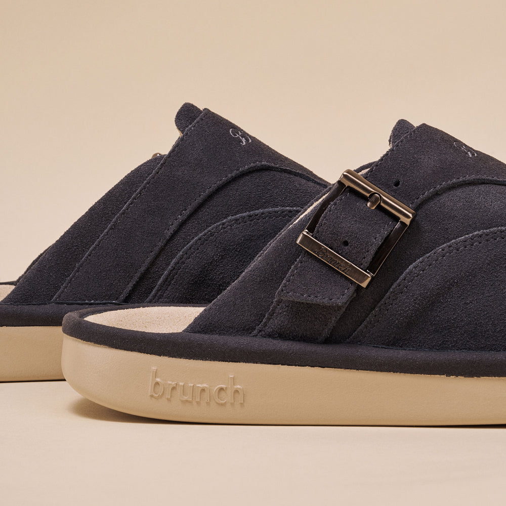 Charcoal suede slide sandal with metal buckle and beige sole embossed 'brunch'.