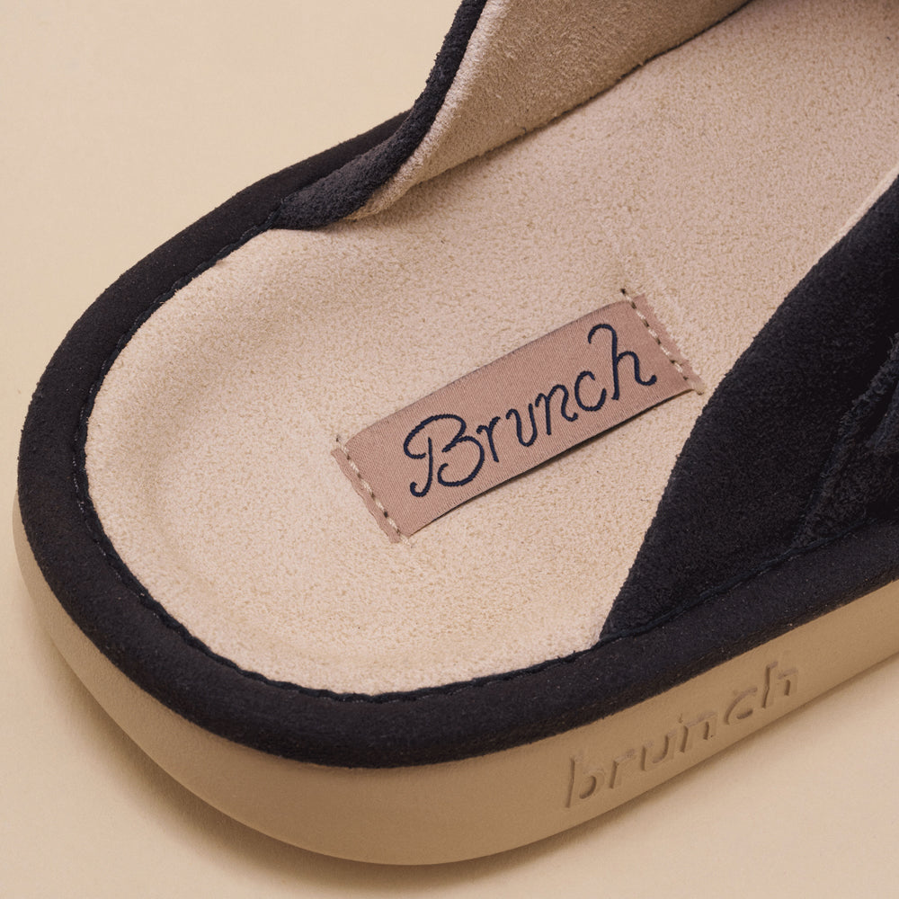 Charcoal suede slipper close-up with stitched label "Brunch" and embossed "brunch" on the sole