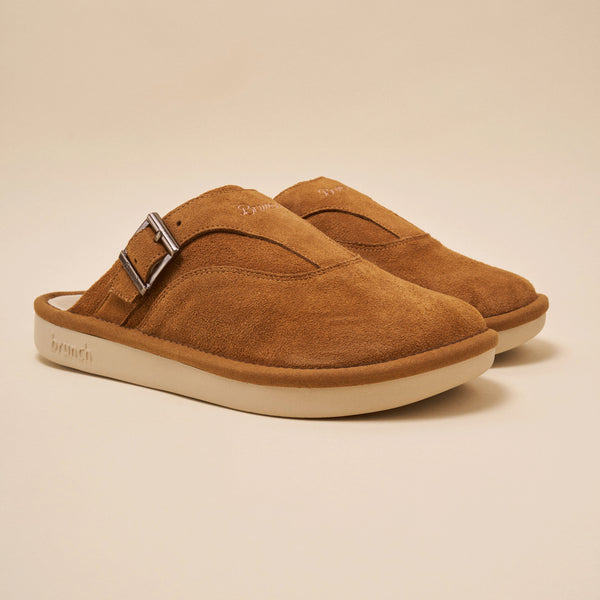 Tan suede slip-on clogs with metal buckle, pair shown angled left; 'brunch' embossed on outer sole.