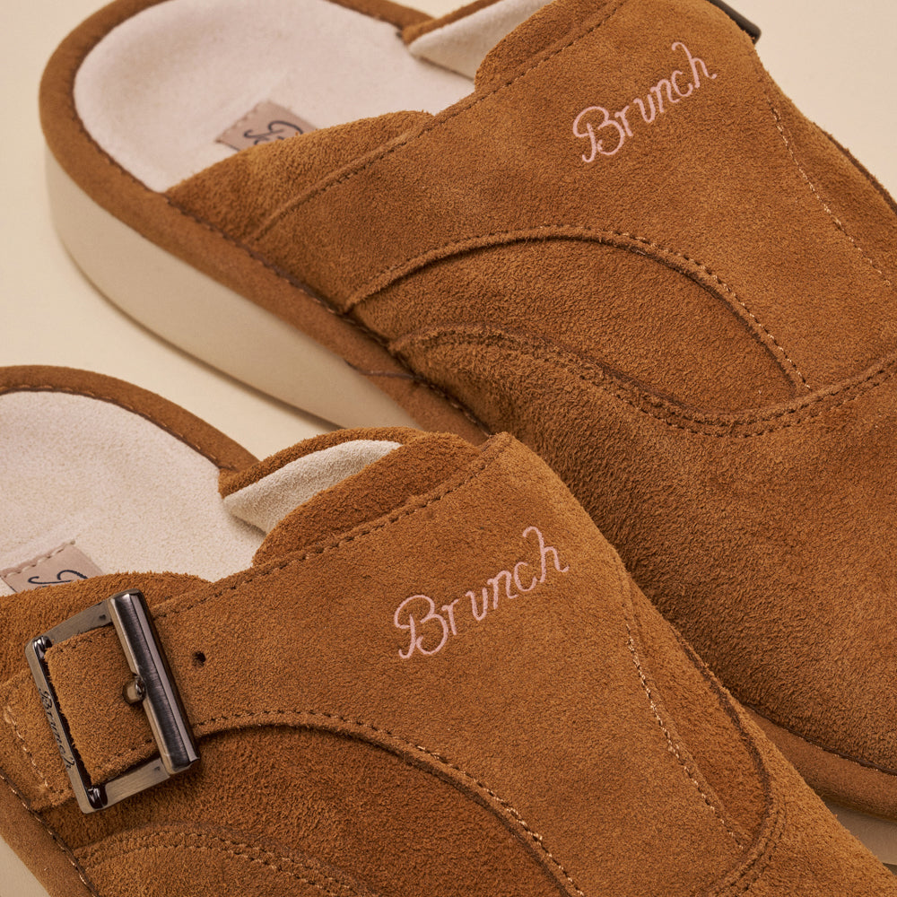 Brown suede mule slippers with embroidered 'Brunch' on the uppers and a metal buckle.