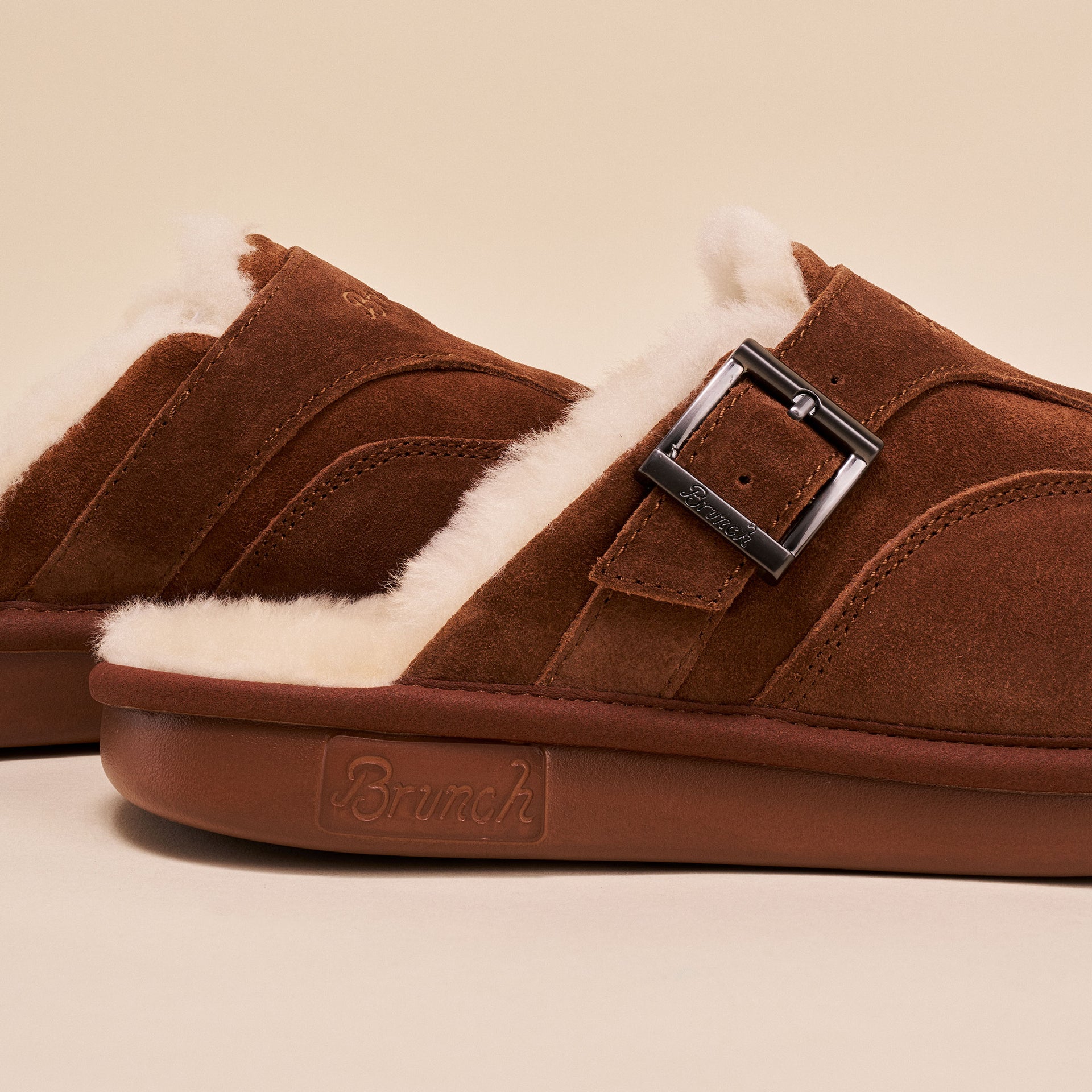 Brown suede mule with shearling lining, metal buckle, and 'Brunch' embossed on the sole.