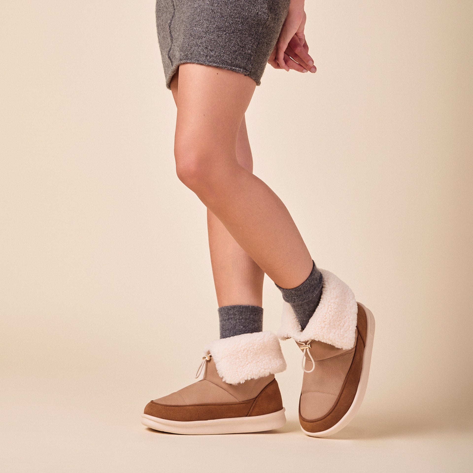 Model wearing camel-colored shearling-lined ankle boots with fold-over cuff and gray socks