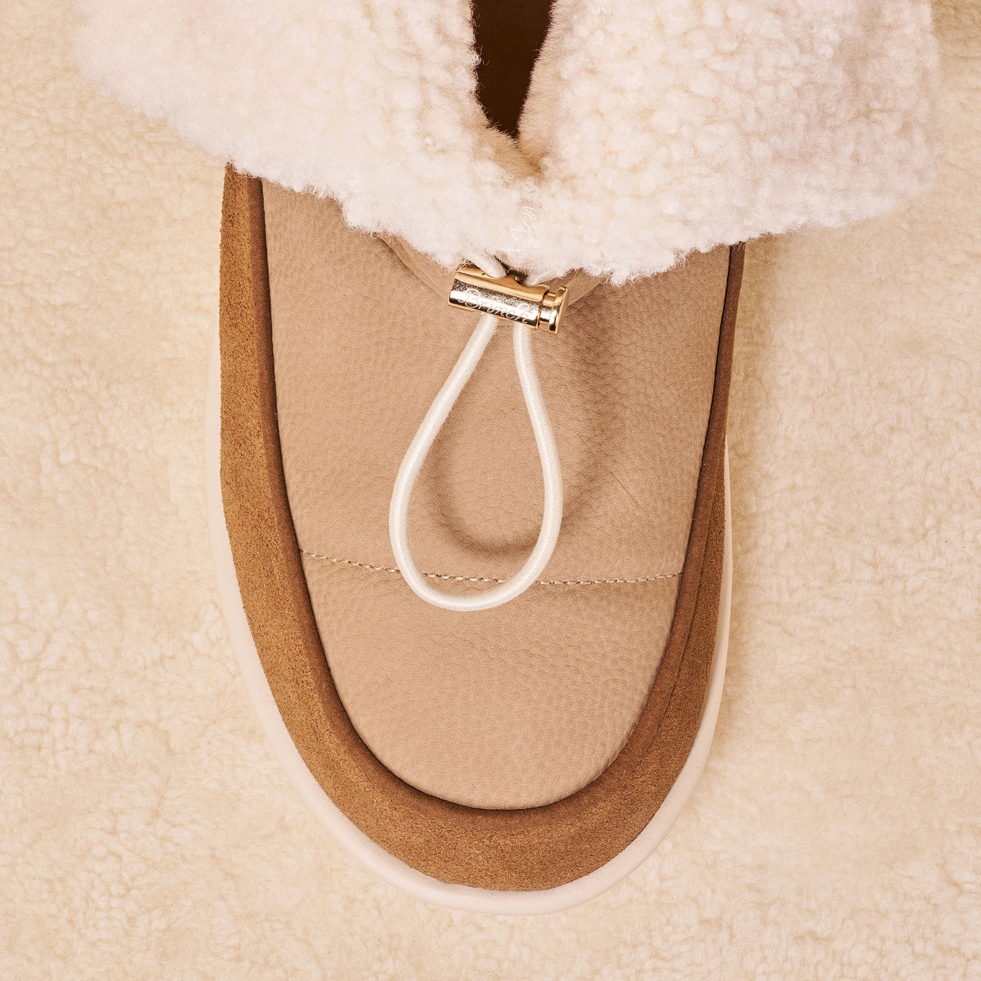 Top of camel shearling-lined slipper showing suede trim, textured leather upper and gold cord toggle