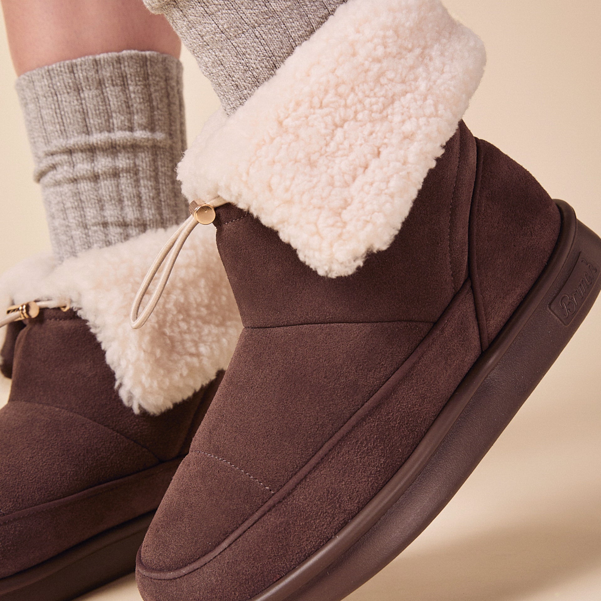 Ankle-height dark brown suede boots with cream shearling cuff, drawcord toggle, and thick rubber sole.