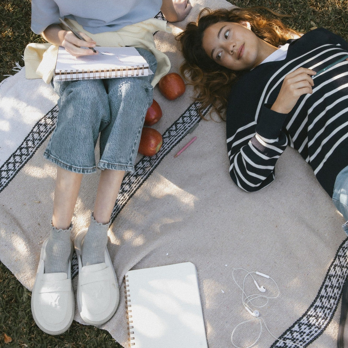 Two people lying on a blanket outdoors with apples and notebooks.