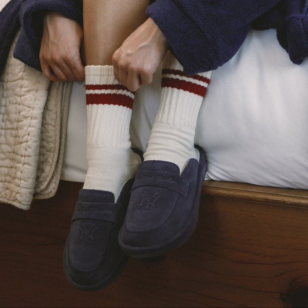 Two people sitting close together wearing matching navy blue pajama sets with white socks and dark shoes.