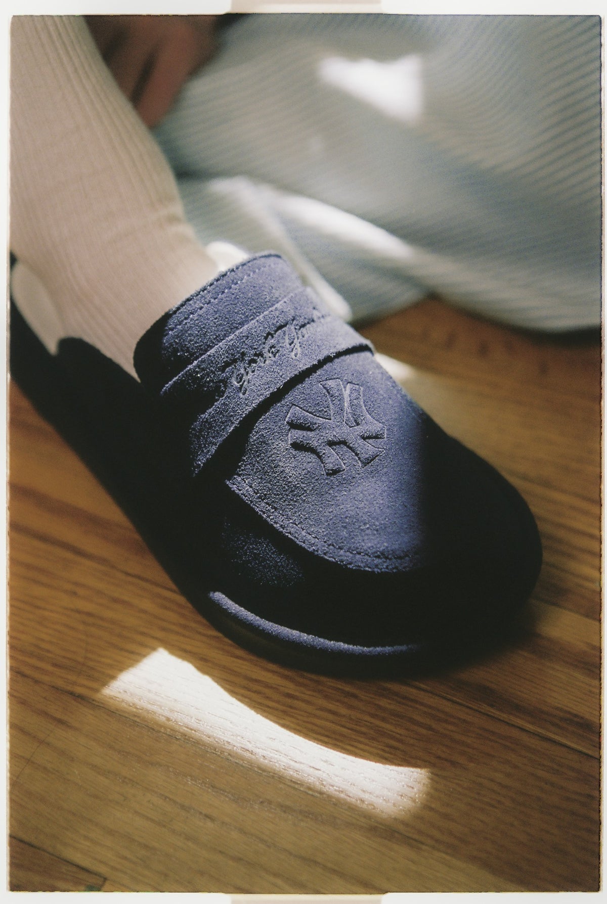 Front close-up of navy suede loafer with embossed Yankees logo and tonal Brunch embroidery on foot with white sock on hardwood