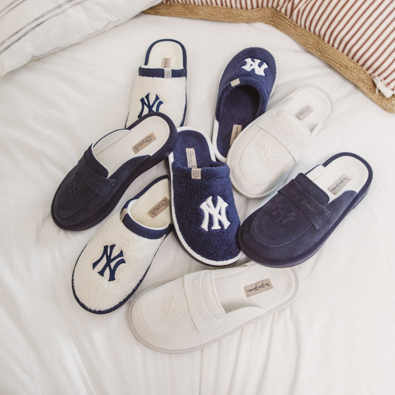 Pair of navy and white slippers with a logo on a bed