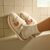 Person wearing white slippers with pink bows against a tiled bathroom wall.