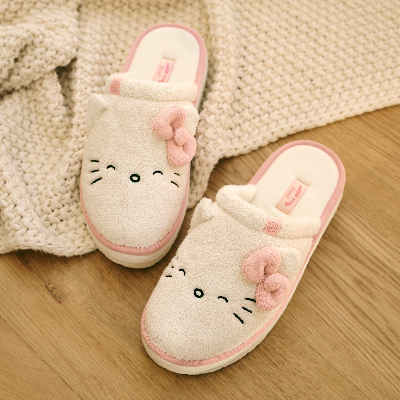 Pair of cartoon slippers with a bow on a wooden floor with a knitted blanket.