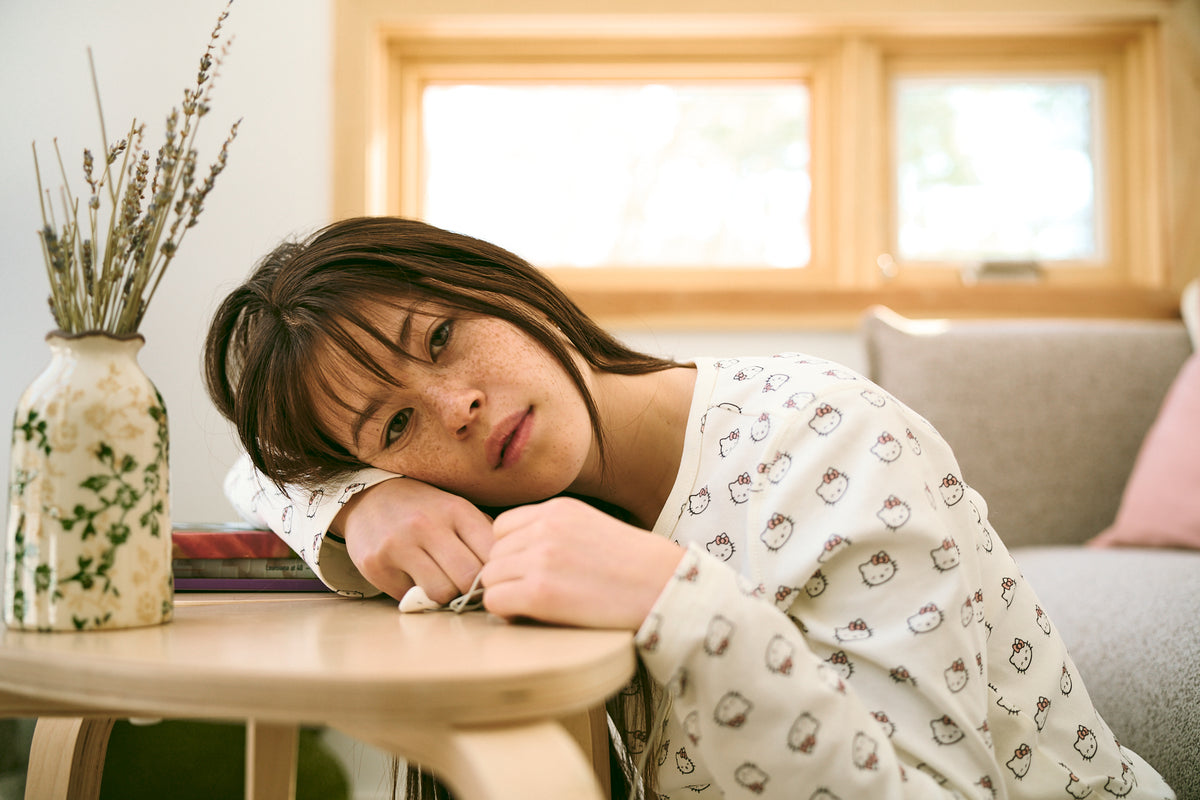 Young woman with freckles resting her head on a table, wearing Hello Kitty–patterned pajamas
