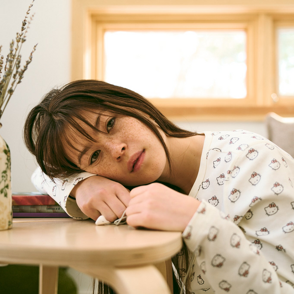 Woman in pajamas leaning on a table in a cozy room with a vase and books.
