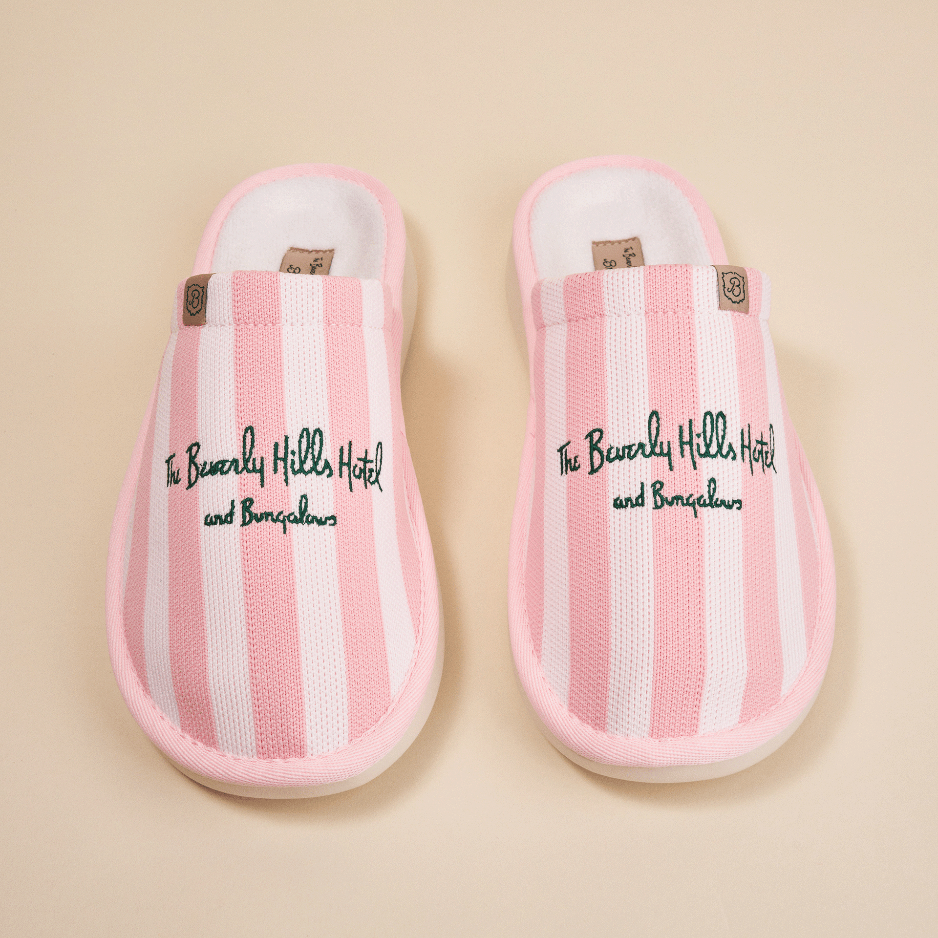 Pink-and-white striped slippers with green embroidered text 'The Beverly Hills Hotel and Bungalows'.