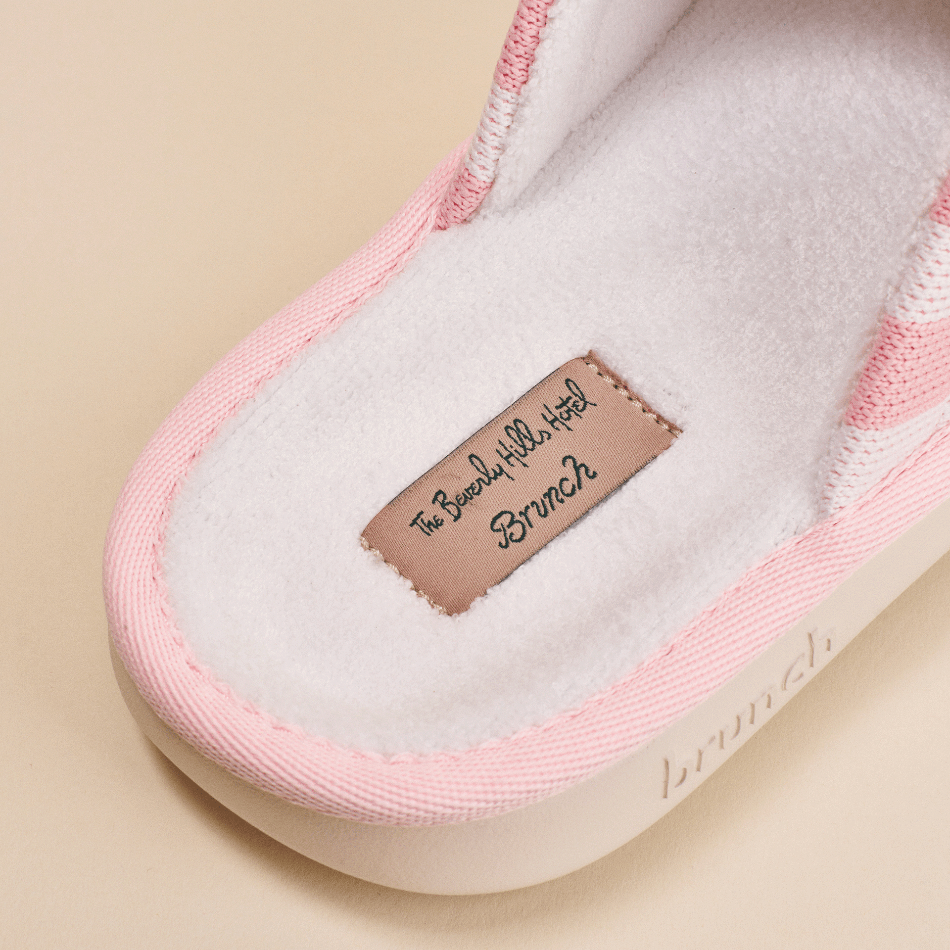 Pink plush slipper close-up showing stitched insole label reading 'The Beverly Hills Hotel Brunch'.