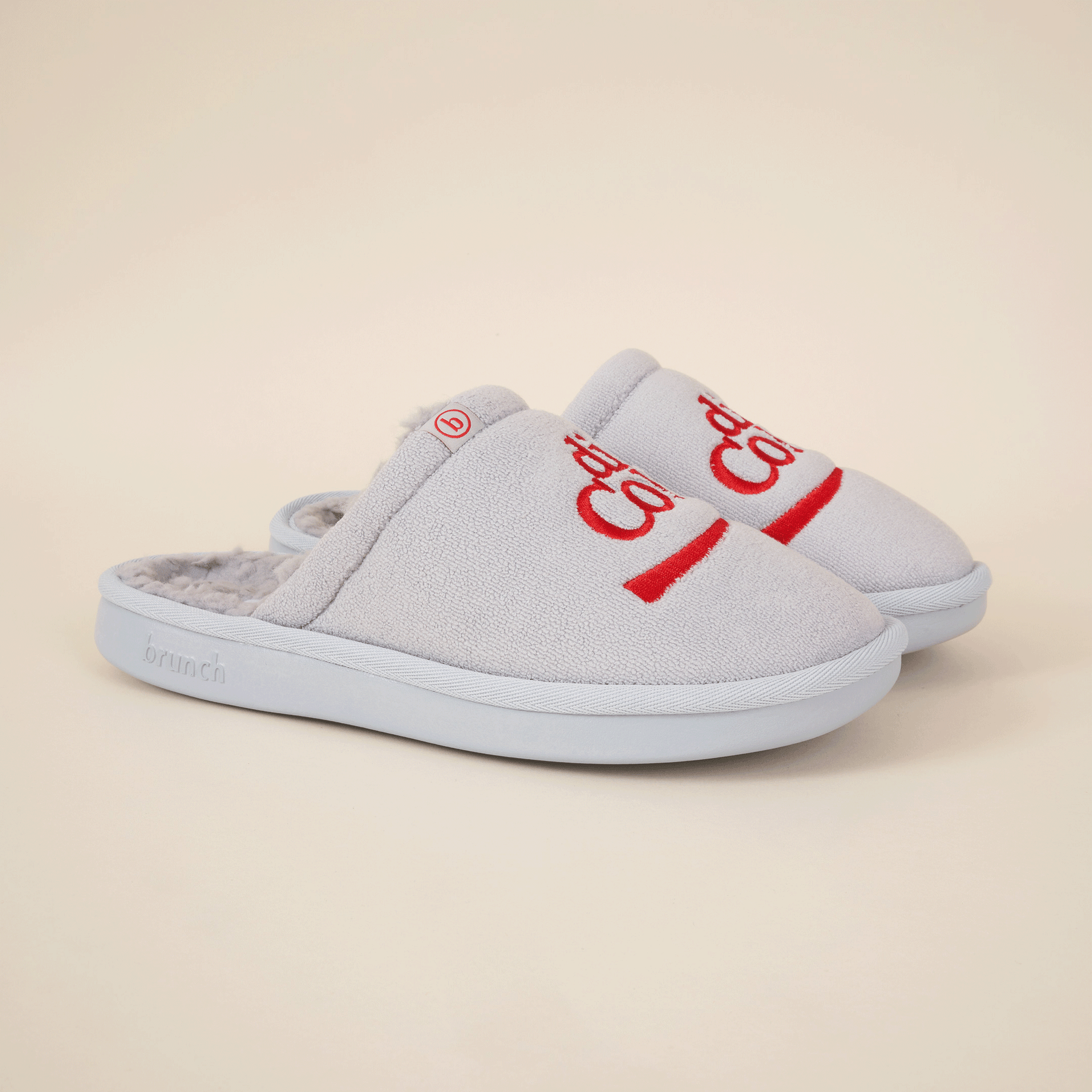 Light grey fleece slip-on slippers with red 'brunch' embroidery, small red 'b' tag, and embossed 'brunch' on sole