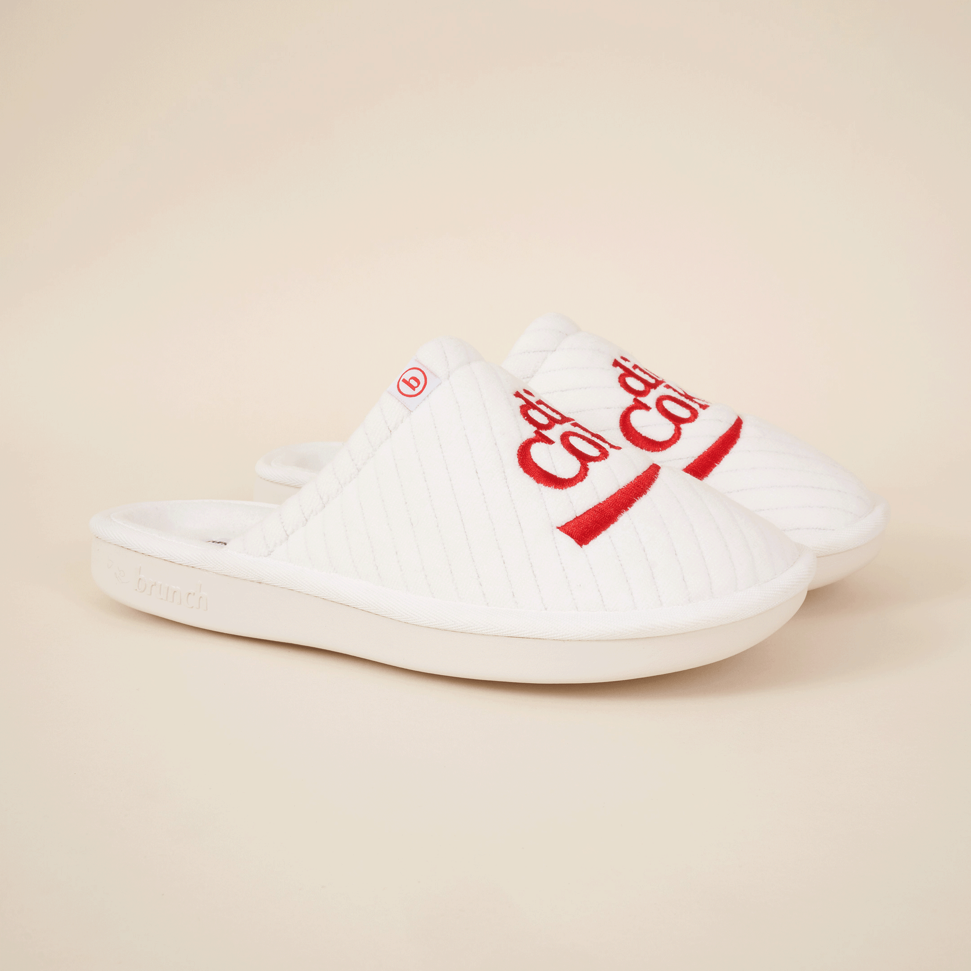 White quilted slip-on slippers with red embroidery, small 'b' tag and 'brunch' embossed on sole.