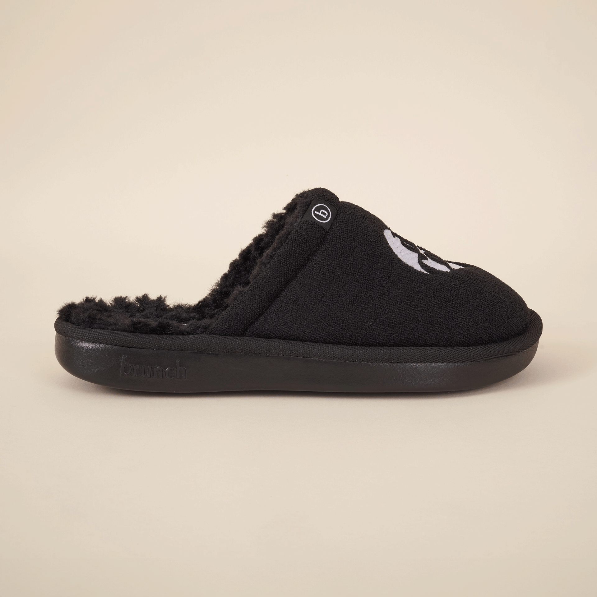 Black slip-on fuzzy slipper with embroidered face on top and 'brunch' embossed on the sole.