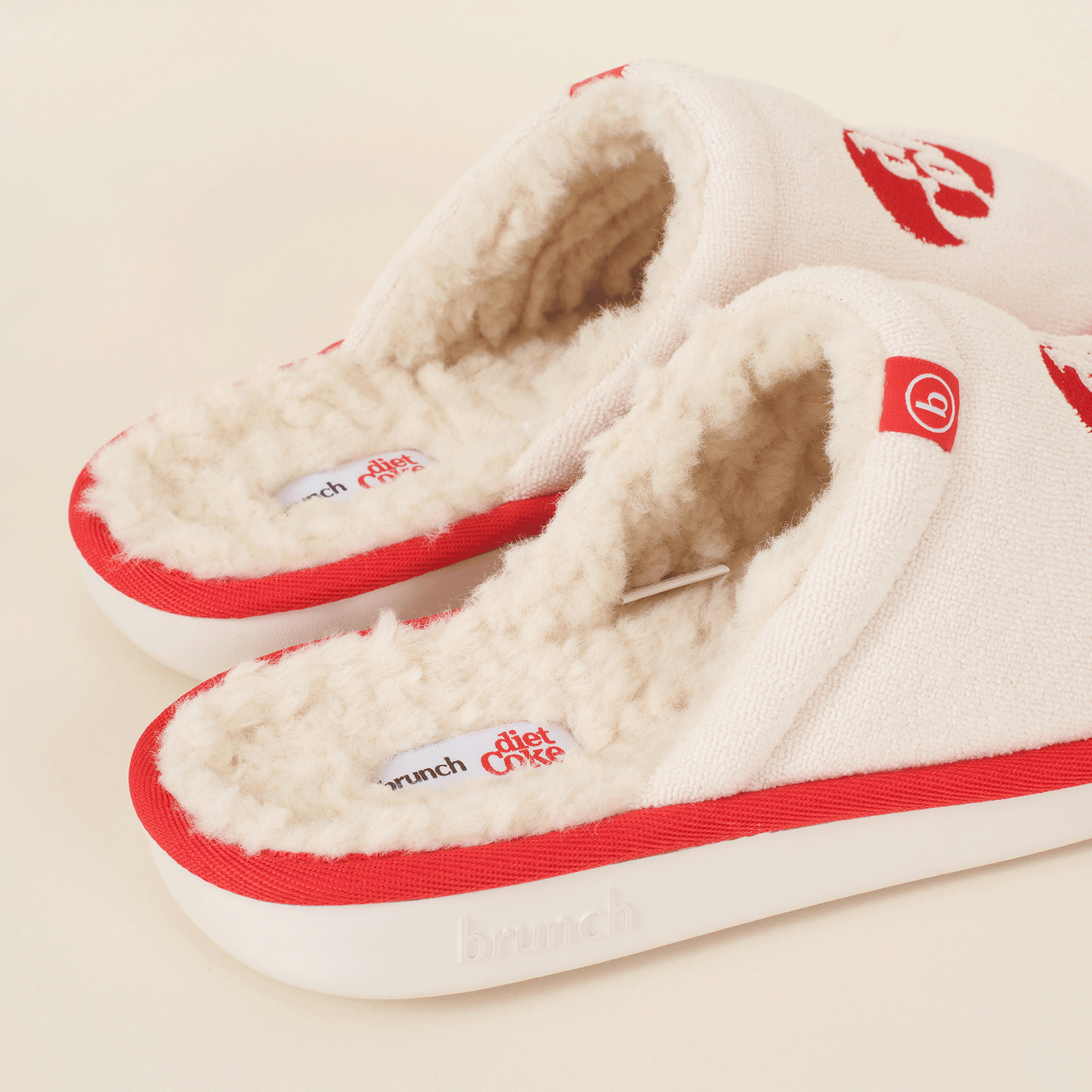Cream fuzzy slip-on slippers with red trim; "brunch" embossed on sole and insole label reading "diet coke".