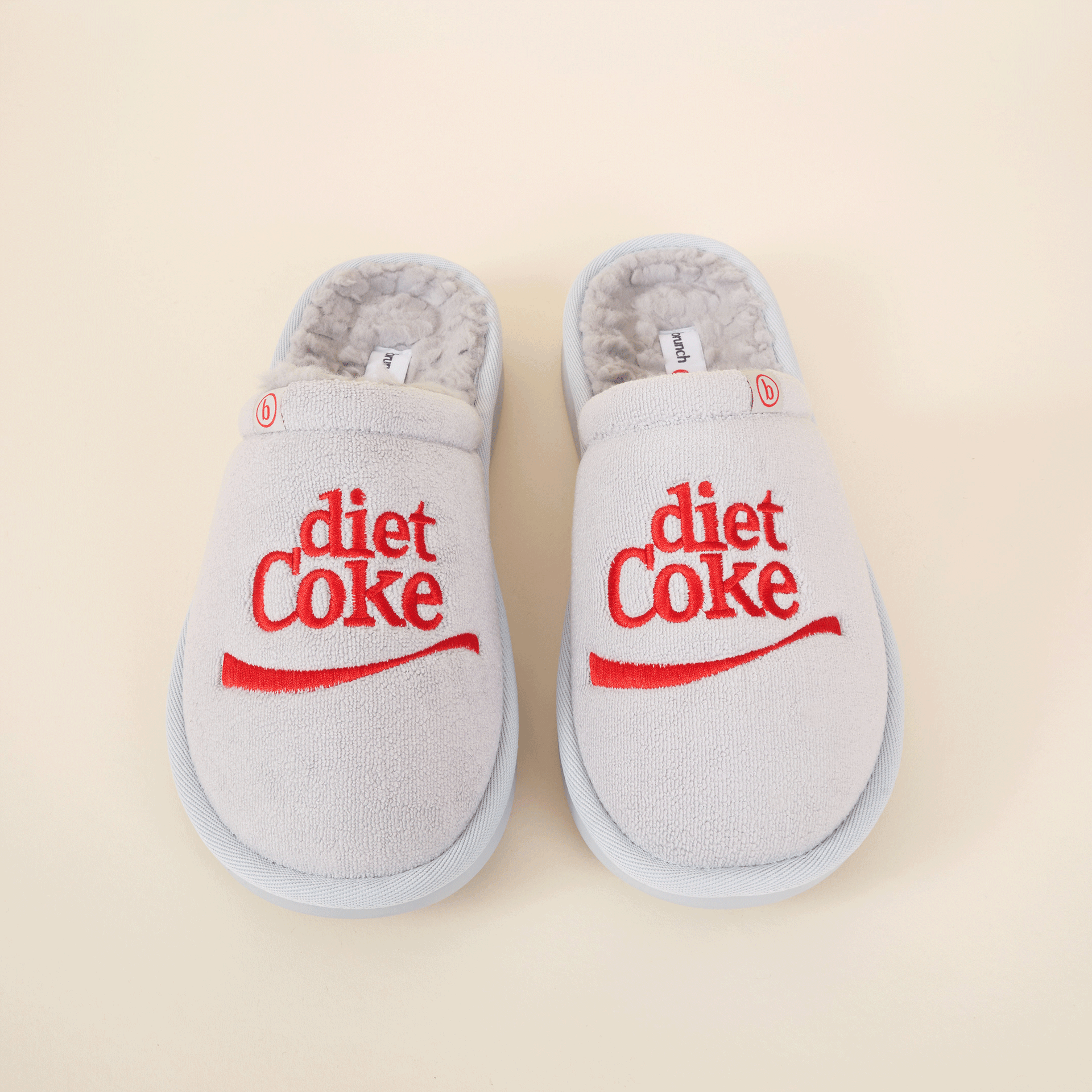 Pair of light grey plush slippers with red 'diet Coke' logo embroidered on each