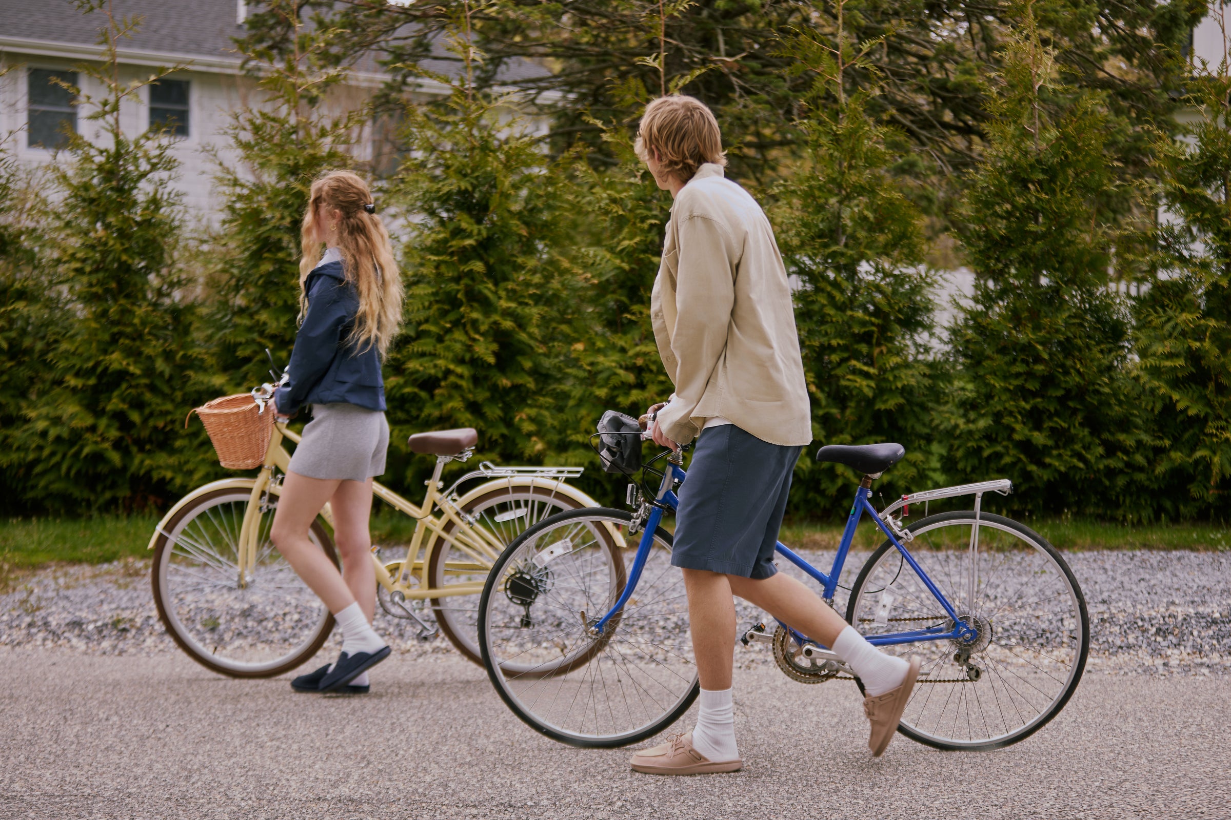 Two people with bicycles walking on a path in a residential area.