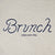 Heathered grey sweatshirt with navy embroidered script 'Brunch' and small text 'enjoy your stay'.