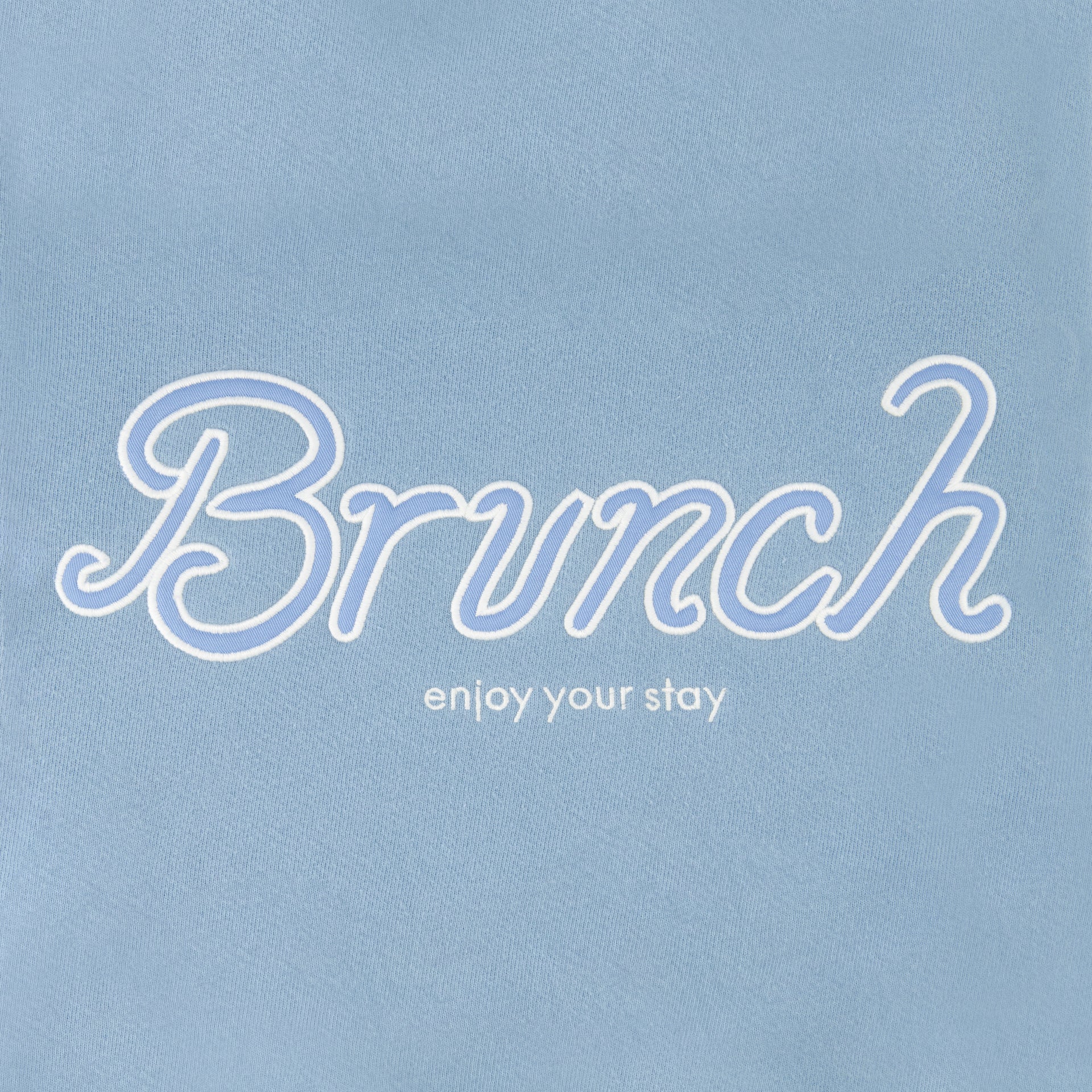 Powder blue sweatshirt front showing white-outlined script 'Brunch' with smaller text 'enjoy your stay'.