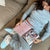 Person in light-blue patterned pajamas and slippers (slipper shows 'Zzz') reading a cookbook on a couch; open page titled 'Grind by day'.