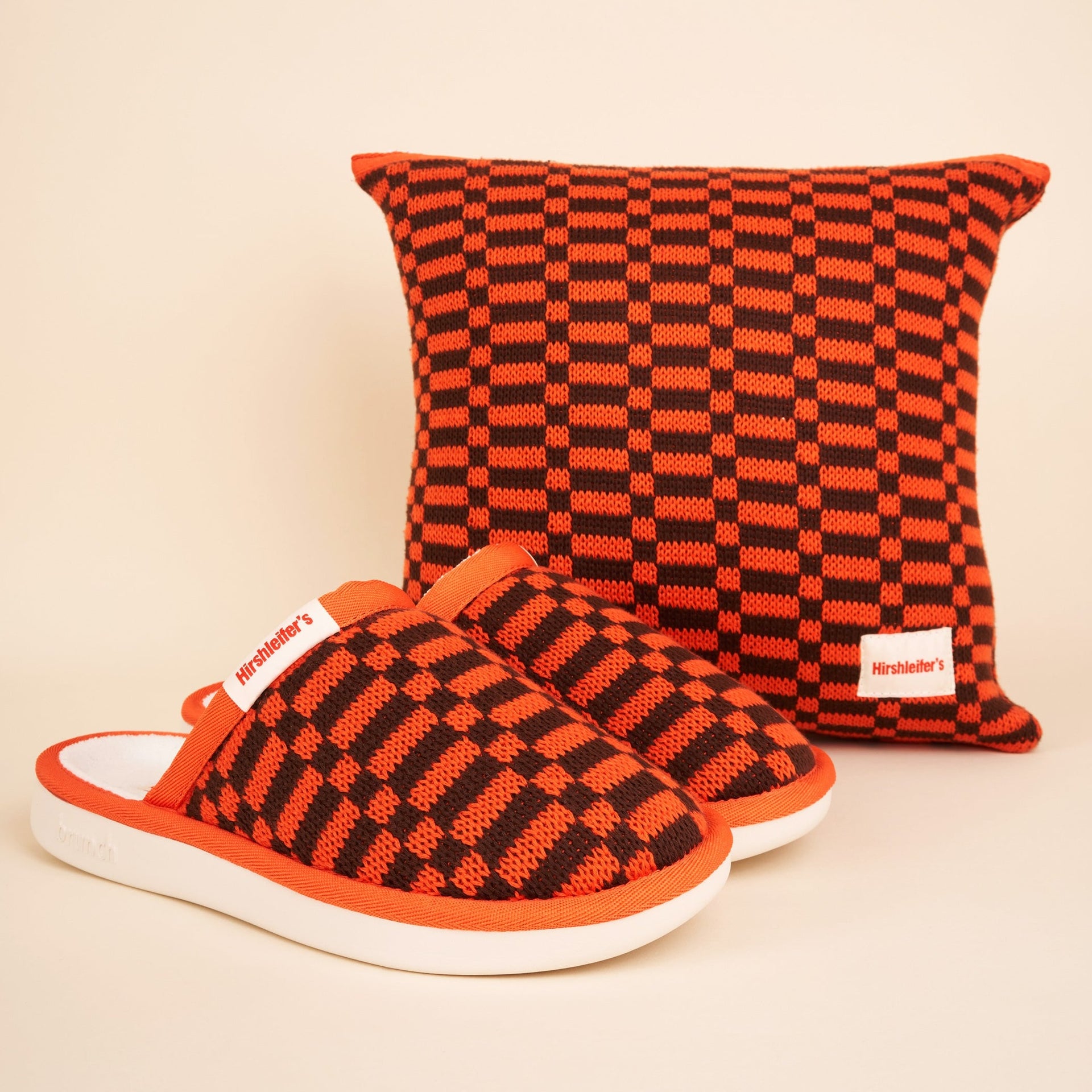 Orange-and-black checkered knit slippers with white soles and matching square pillow, both tagged 'Hirshleifer's'.