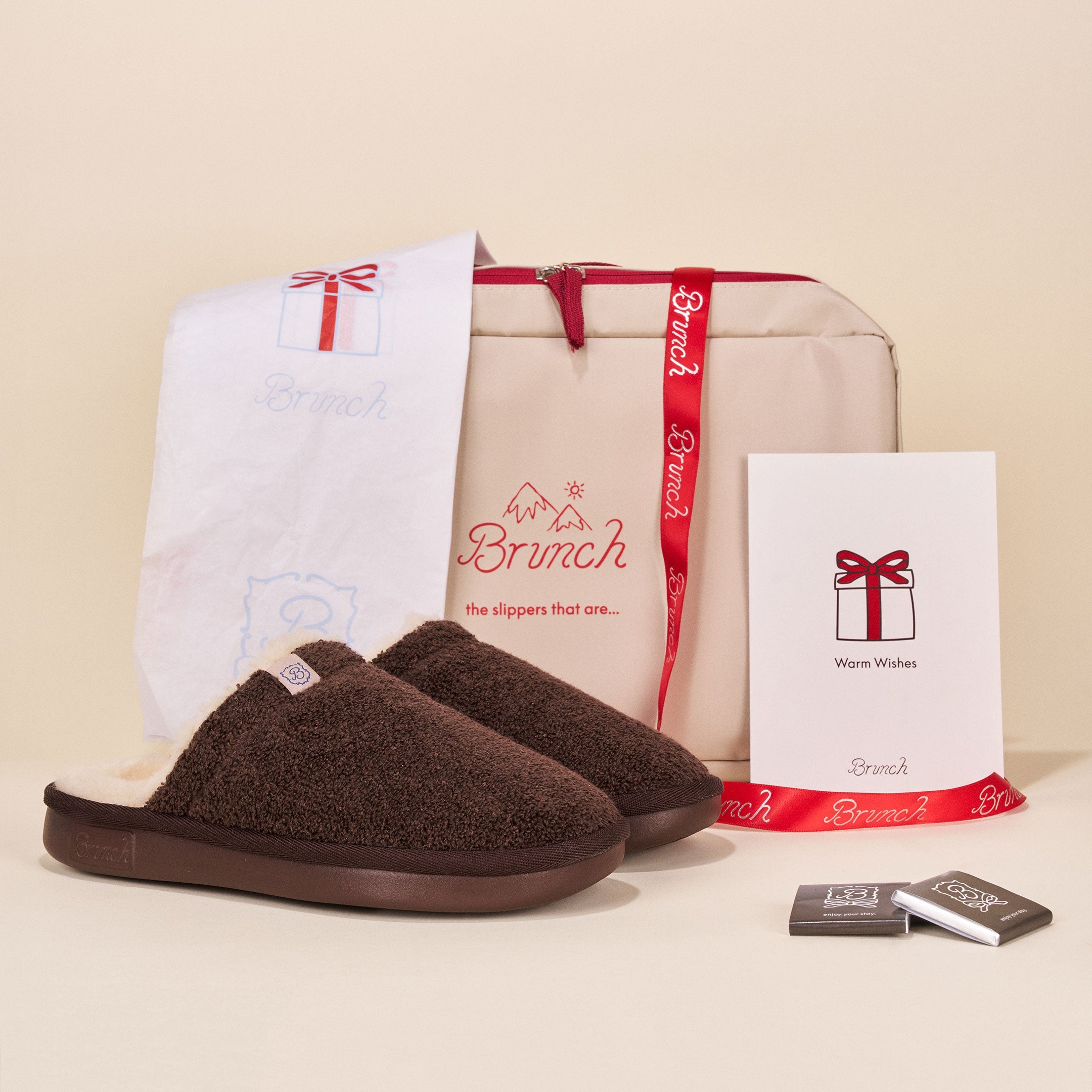Brown slippers with a branded box and gift card on a beige background