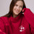 Woman wearing a red sweatshirt with a logo, sitting against a plain background