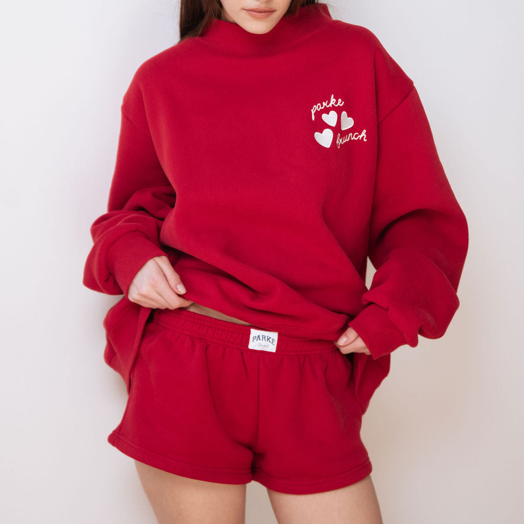 Person wearing a red sweatshirt and shorts set with a logo on a white background