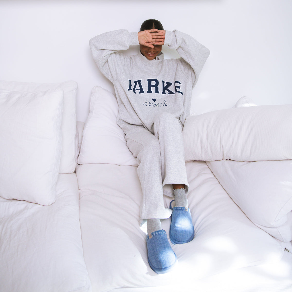 Person sitting on a bed wearing a sweatshirt with 'Bark' printed on it, in a room with a shelf of books.