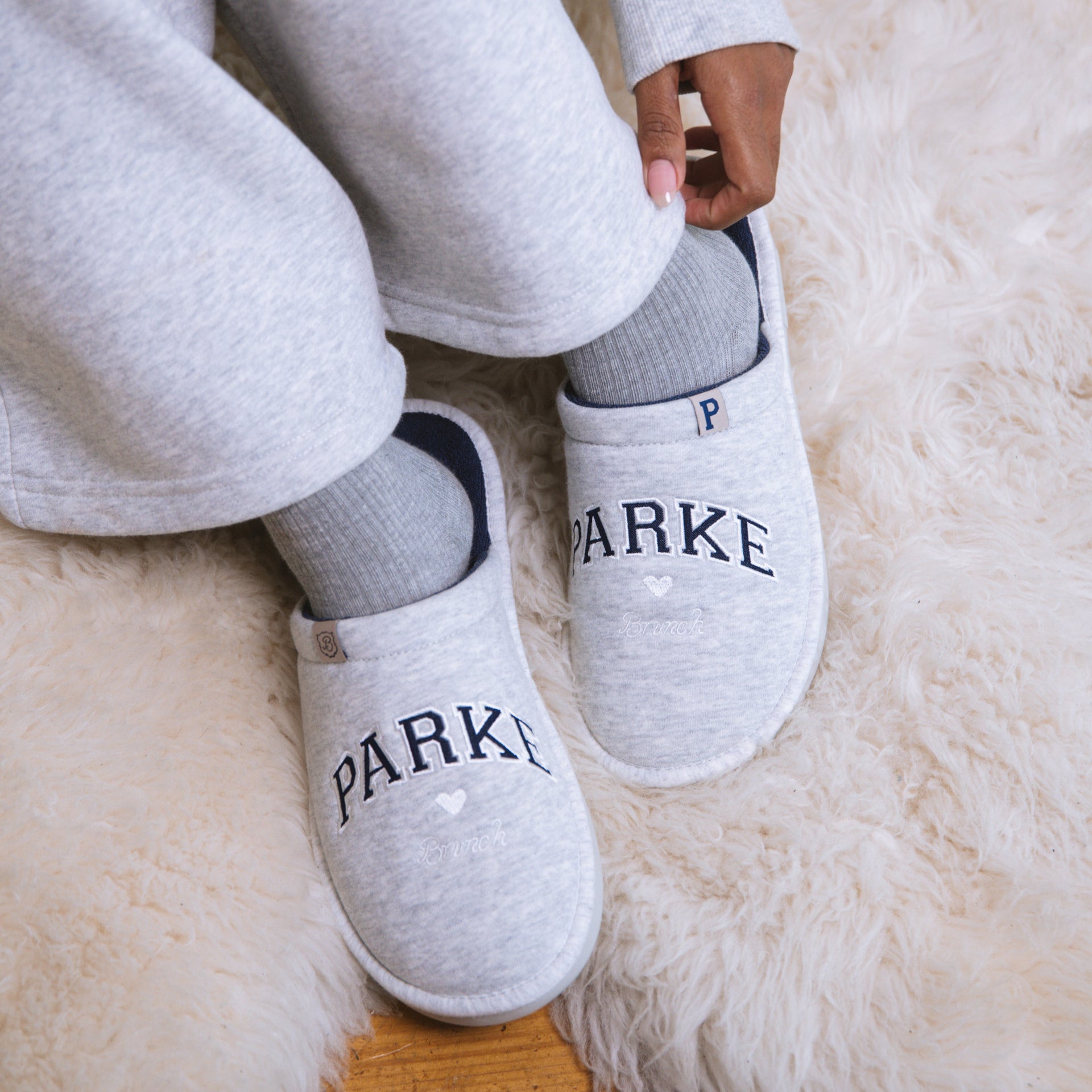 Person wearing gray slippers with 'PARKE' branding on a fluffy white surface.