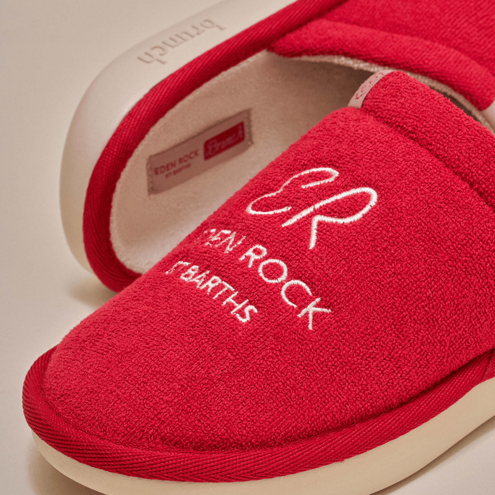 Red terry-cloth slipper with embroidered ER logo and text 'EDEN ROCK ST BARTHS' on the toe.
