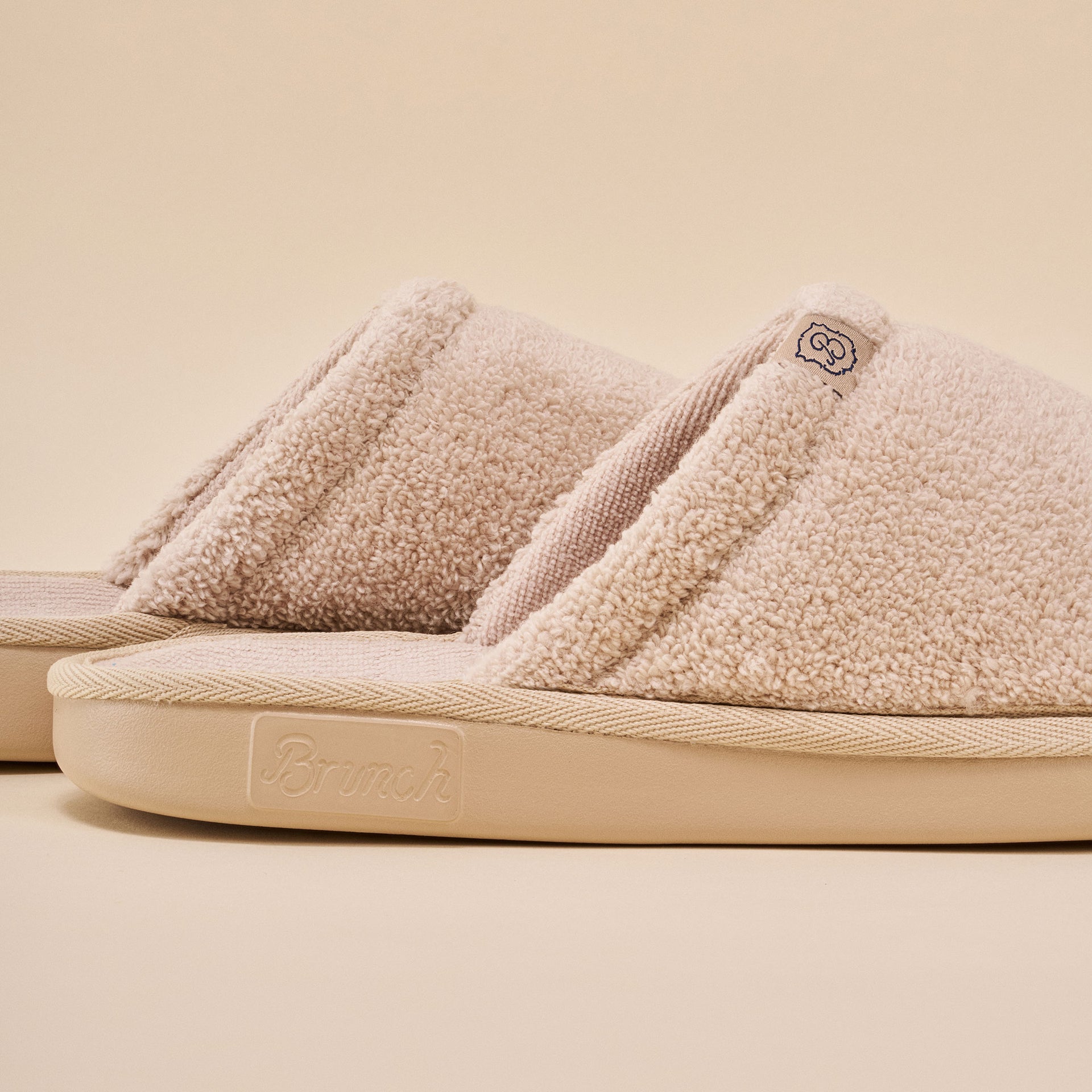 Beige sherpa-lined slide slippers with 'Brunch' embossed on the sole.