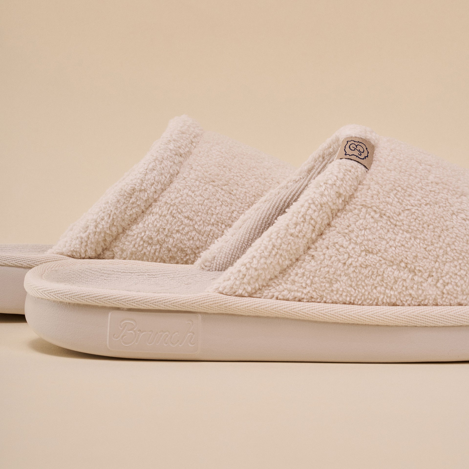 Cream sherpa slide slipper with "Brunch" embossed on the sole.