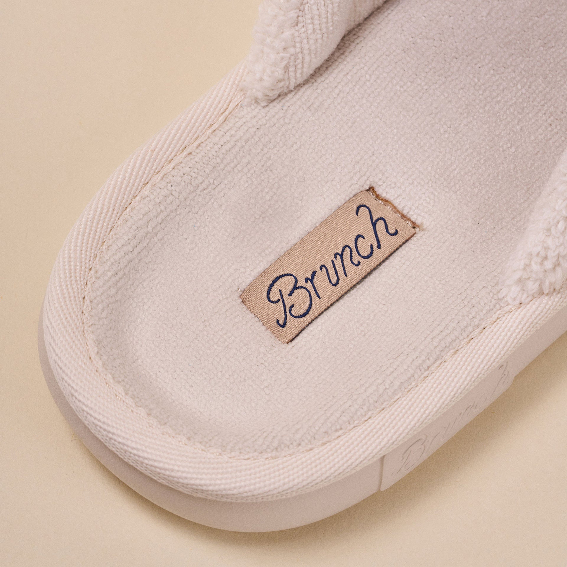 Cream fabric slipper insole close-up showing sewn label reading 'Brunch'